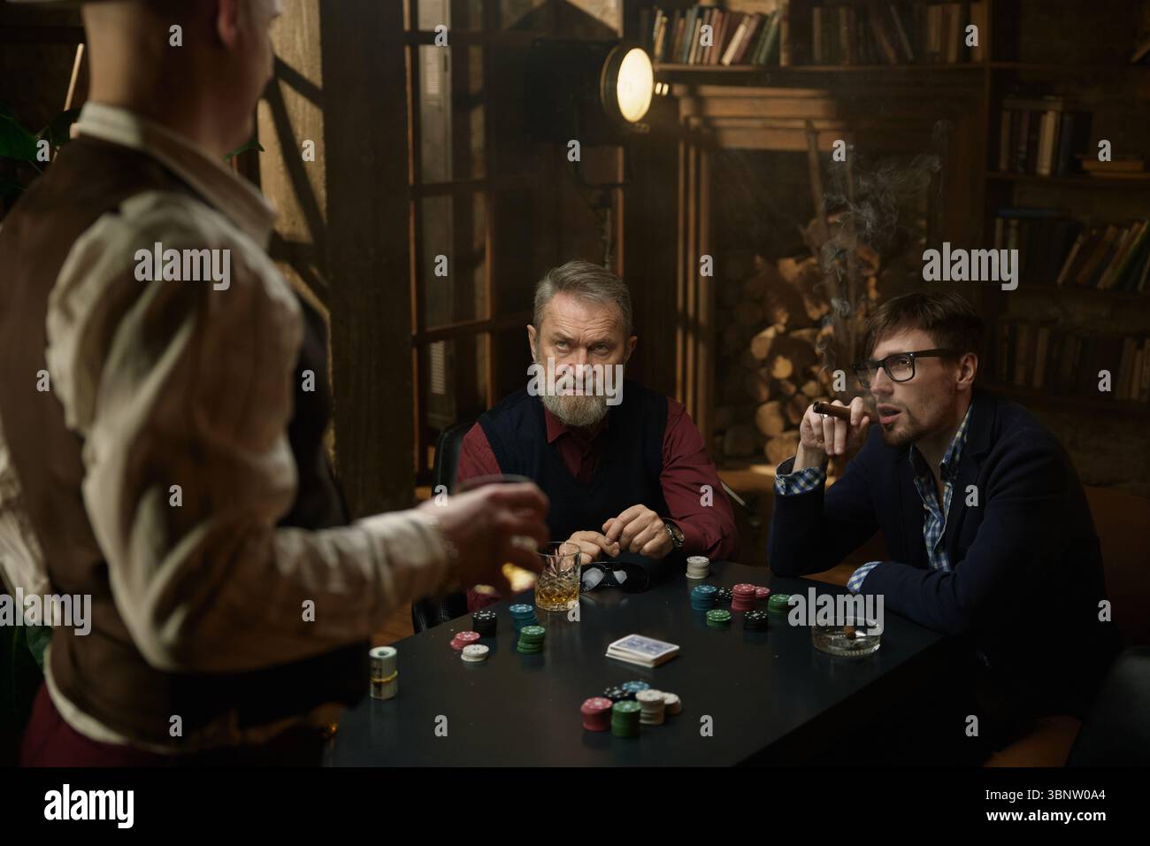 Tre uomini che si divertono a giocare a poker si svolgono in un ambiente vintage splendidamente decorato Foto Stock