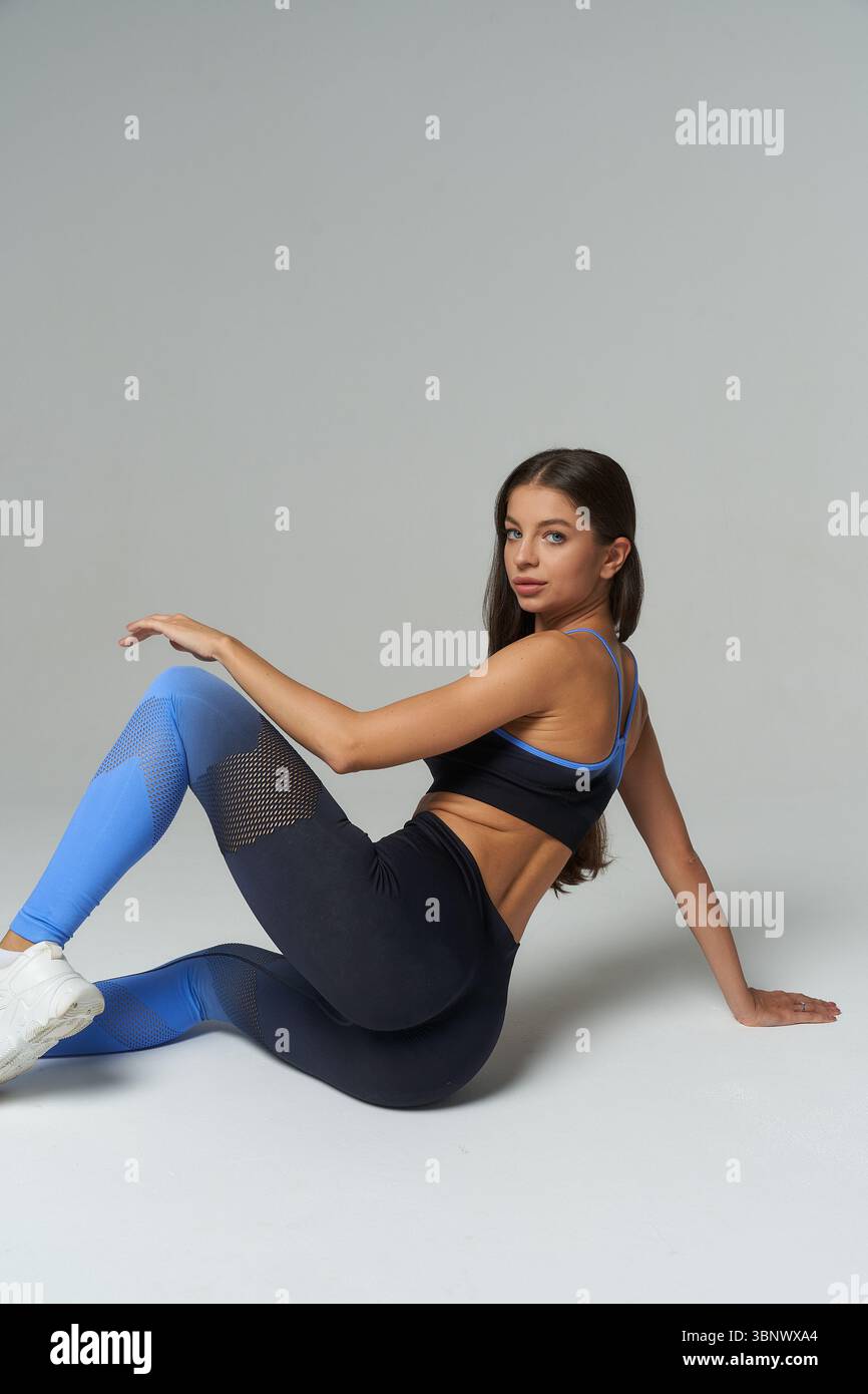 Una donna atletica indossa leggings blu e neri con dettagli in mesh e un reggiseno sportivo coordinato. Ha lunghi capelli scuri e.. Foto Stock