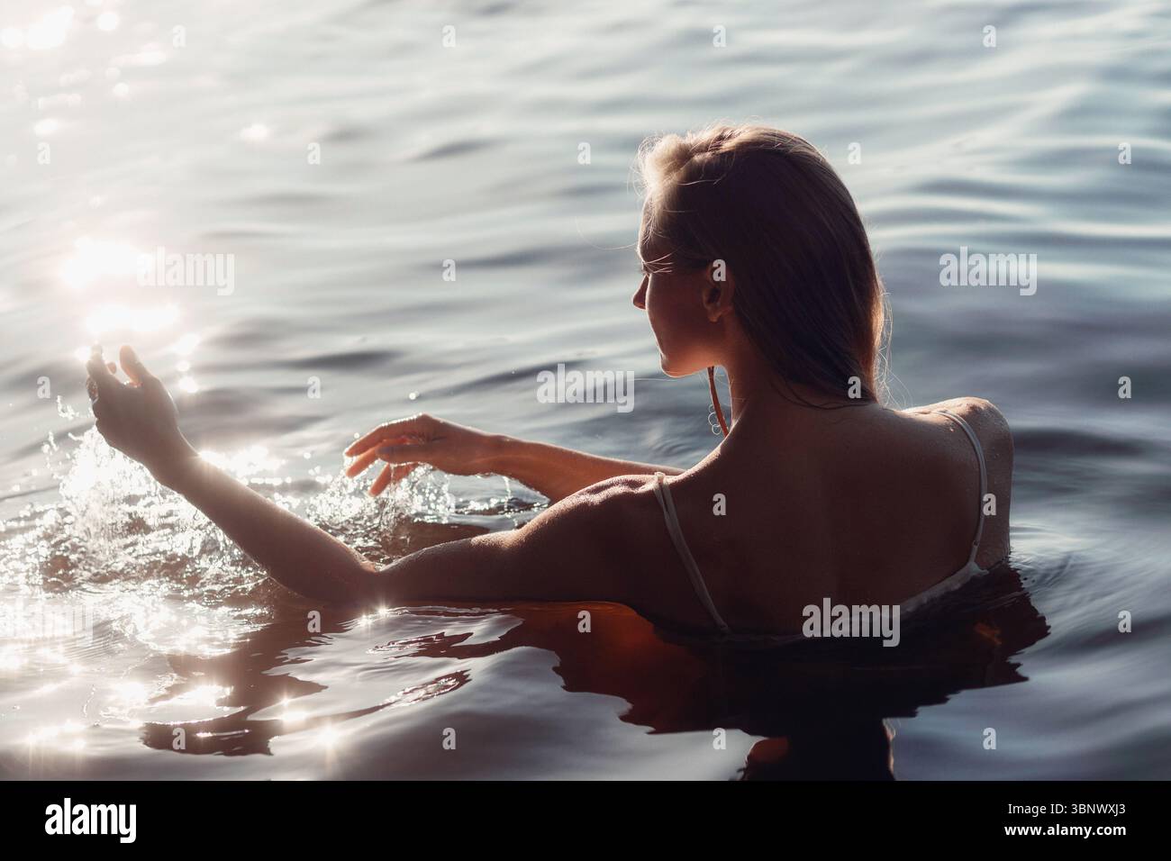In un lago tranquillo, una donna cammina attraverso l'acqua calma, spruzzando giocosamente con una mano mentre sperimenta un momento tranquillo durante il tu dorato Foto Stock