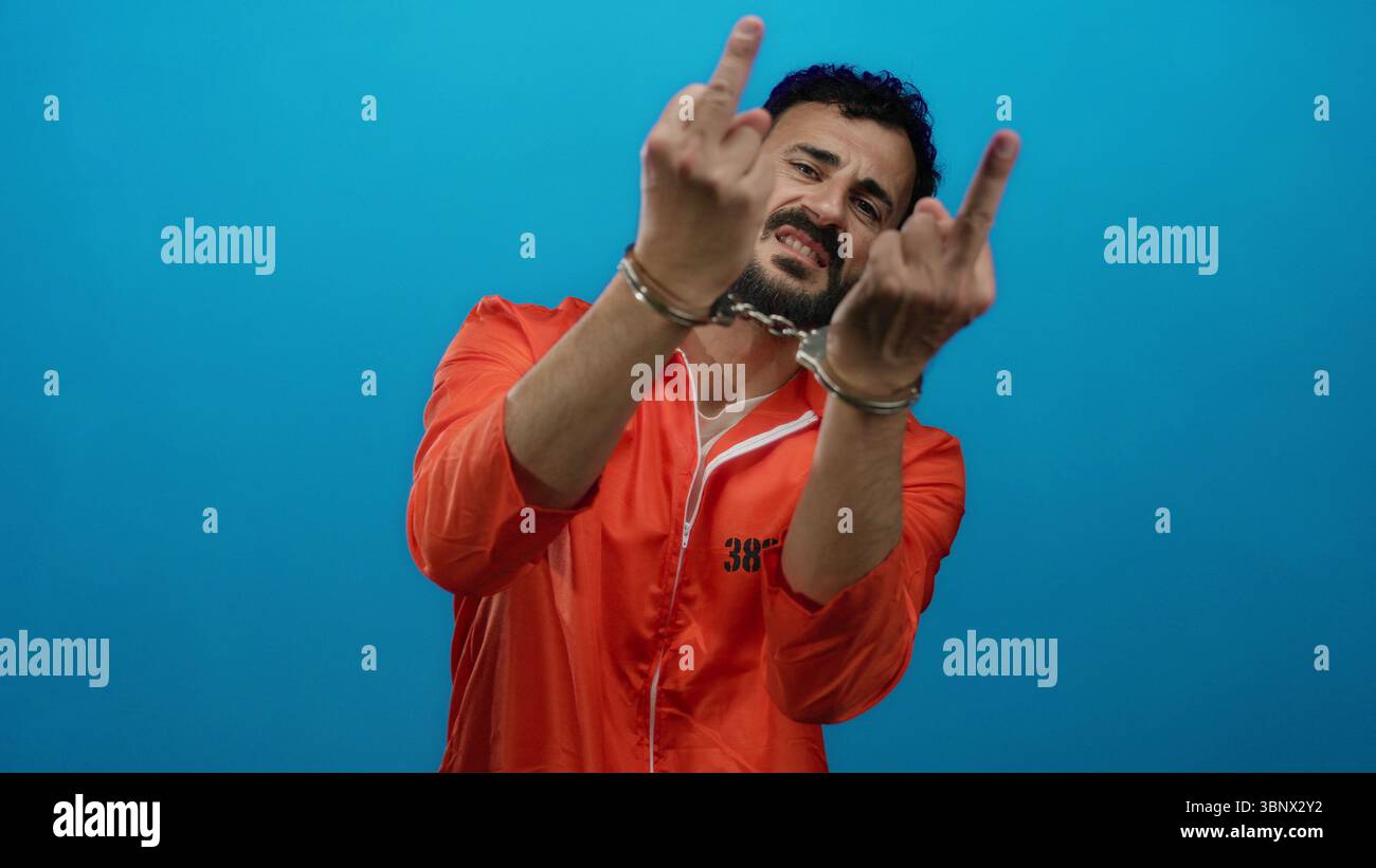 L'uomo ispanico in prigione arancione indossa una tuta con manette su sfondo blu che trasmette una scena drammatica di incarcerazione e sfida. Foto Stock
