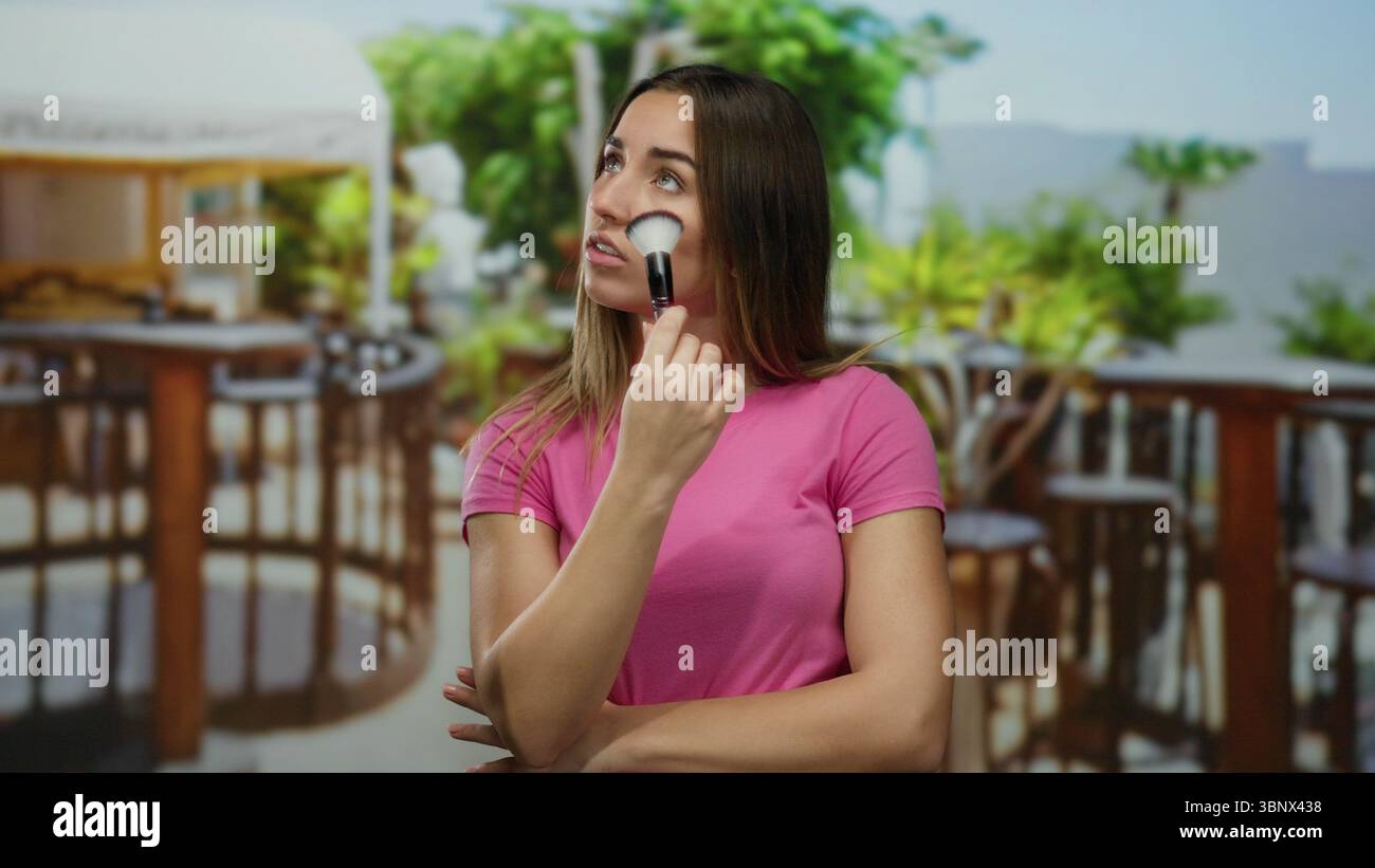 Donna che tiene in mano un pennello per il trucco sulla terrazza del ristorante, ponendo sotto il cielo limpido all'aperto, mescolando pensiero e bellezza Foto Stock