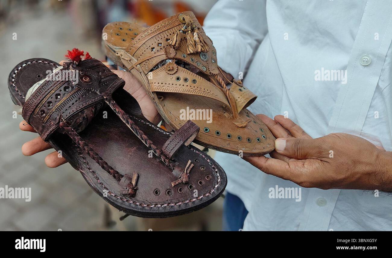 Un negoziante mostra un paio di palle Kolhapuri (sandali indiani artigianali) tenute in vendita in un negozio di strada. Il marchio italiano di moda di lusso Prada, che ha lanciato i suoi 'sandali con anello di dito', è accusato di copiare il design ispirato alle zampe Kolhapuri (sandali indiani artigianali) senza dare il dovuto credito agli artigiani indigeni che li hanno creati nel distretto di Kolhapur nel Maharashtra secoli fa. Un contenzioso di interesse pubblico (PIL) è stato depositato presso l'alta Corte di Bombay in cerca di un risarcimento per gli artigiani di Kolhapuri chappall (sandali indiani artigianali) di Prada. Foto Stock