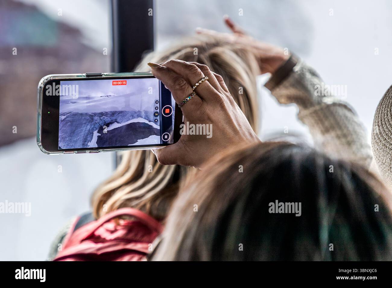 Una donna filma il paesaggio glaciale sotto il Titlis con il suo smartphone mentre la gondola Titlis Rotair sale a 3.020 metri. Numerosi turisti si accalcano nella cabina rotante tenendo in alto i loro telefoni, rendendo a volte più difficile godersi la vista. Wolfenschiessen, Canton Nidwalden, Svizzera. Foto Stock