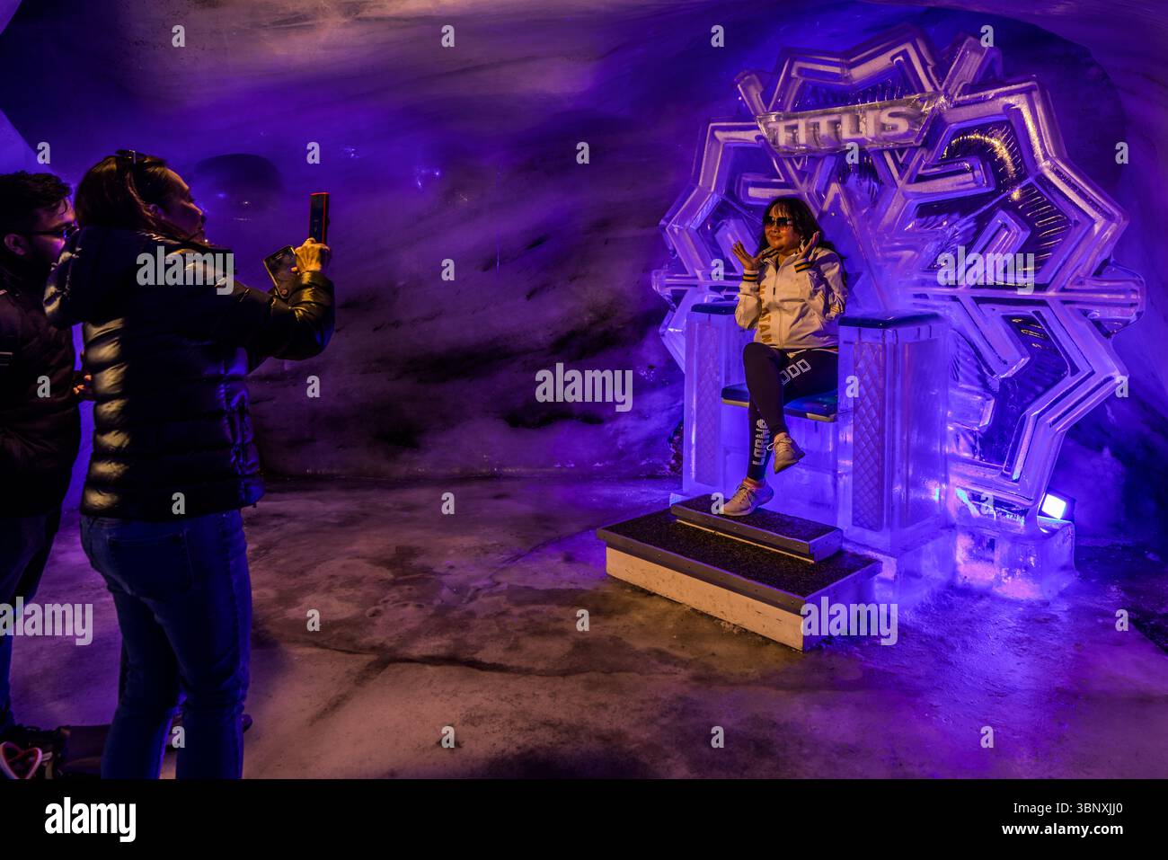 La Grotta del Ghiacciaio del Titlis è un'attrazione turistica a un'altitudine di oltre 3.000 metri, situata direttamente alla stazione della funivia del Titlis. La grotta è costituita da un passaggio di circa 150 metri, creato artificialmente, che conduce a circa 20 metri sotto la superficie del ghiacciaio. Il tunnel presenta punti fotografici come un trono fatto di ghiaccio eterno. I visitatori posano e scattano foto di se stessi nell'imponente grotta di ghiaccio blu sul Titlis a Engelberg, Obwalden, Svizzera. La scultura di ghiaccio "TITLIS" funge da sfondo suggestivo per le foto ricordo, mentre altri ospiti captu Foto Stock