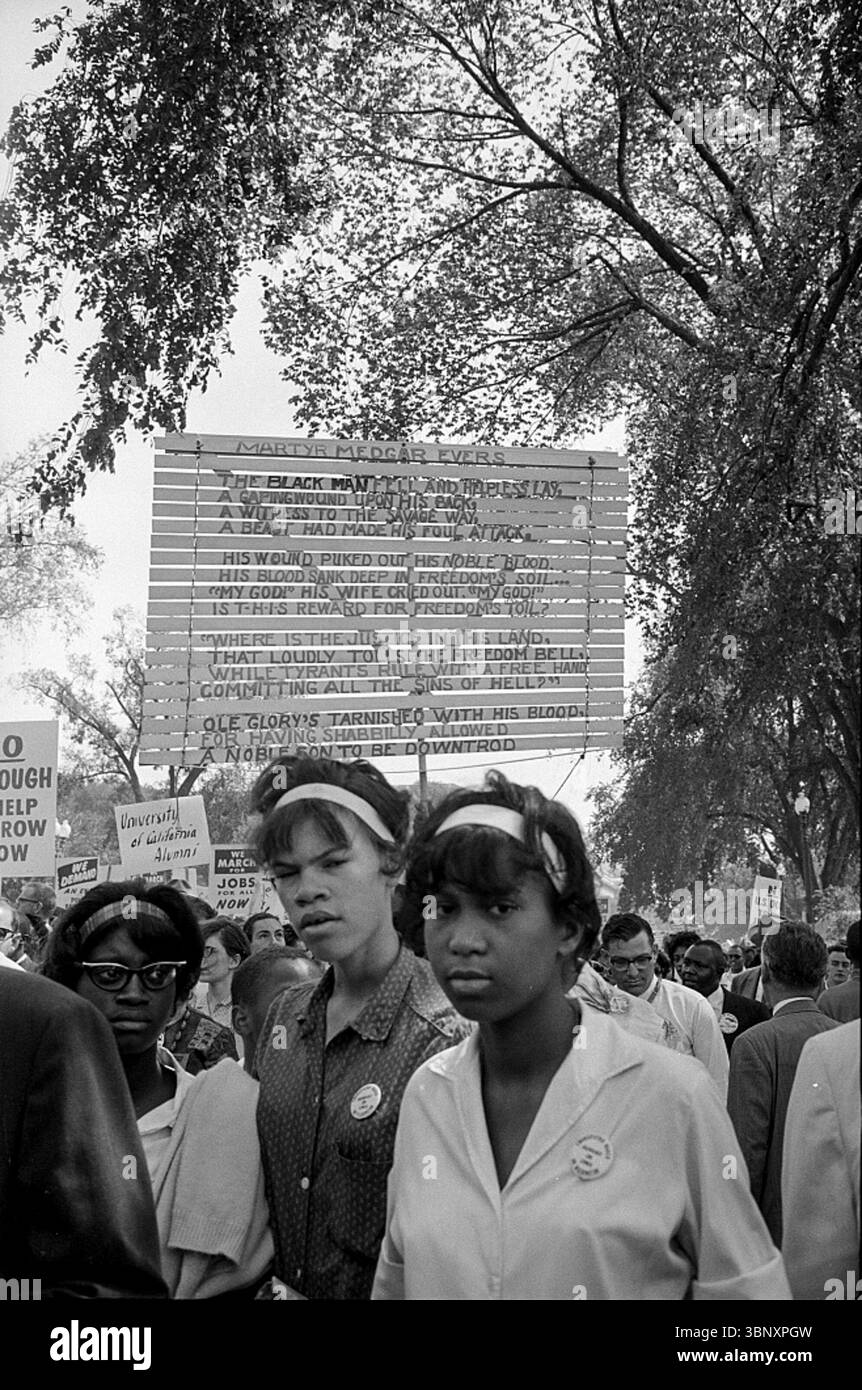La fotografia scattata il 28 agosto 1963 mostra le giovani donne che partecipano alla storica marcia su Washington per il lavoro e la libertà. Dietro di loro è visibile un grande segno in onore di Medgar Evers, un attivista per i diritti civili assassinato nel giugno 1963. L'immagine cattura il forte senso di solidarietà e urgenza per la giustizia e l'uguaglianza tra i manifestanti dei diritti civili a Washington, D.C. Foto Stock