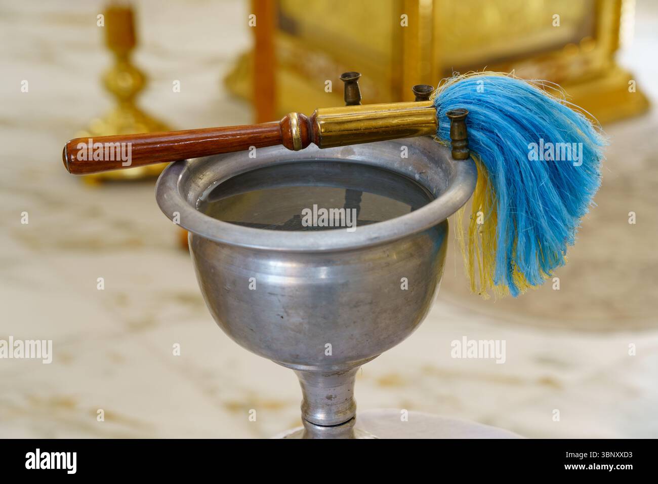 Un bacino metallico pieno d'acqua si trova su una superficie di marmo, accompagnato da un pennello colorato. Questa configurazione riflette un rituale tradizionale durante un evento culturale Foto Stock