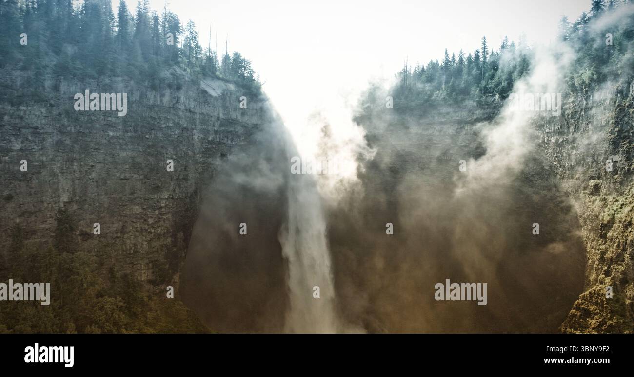 La scenografia a cascata dal design piatto mostra una cascata retroilluminata che si tuffa nel canyon, con alberi sempreverdi Foto Stock