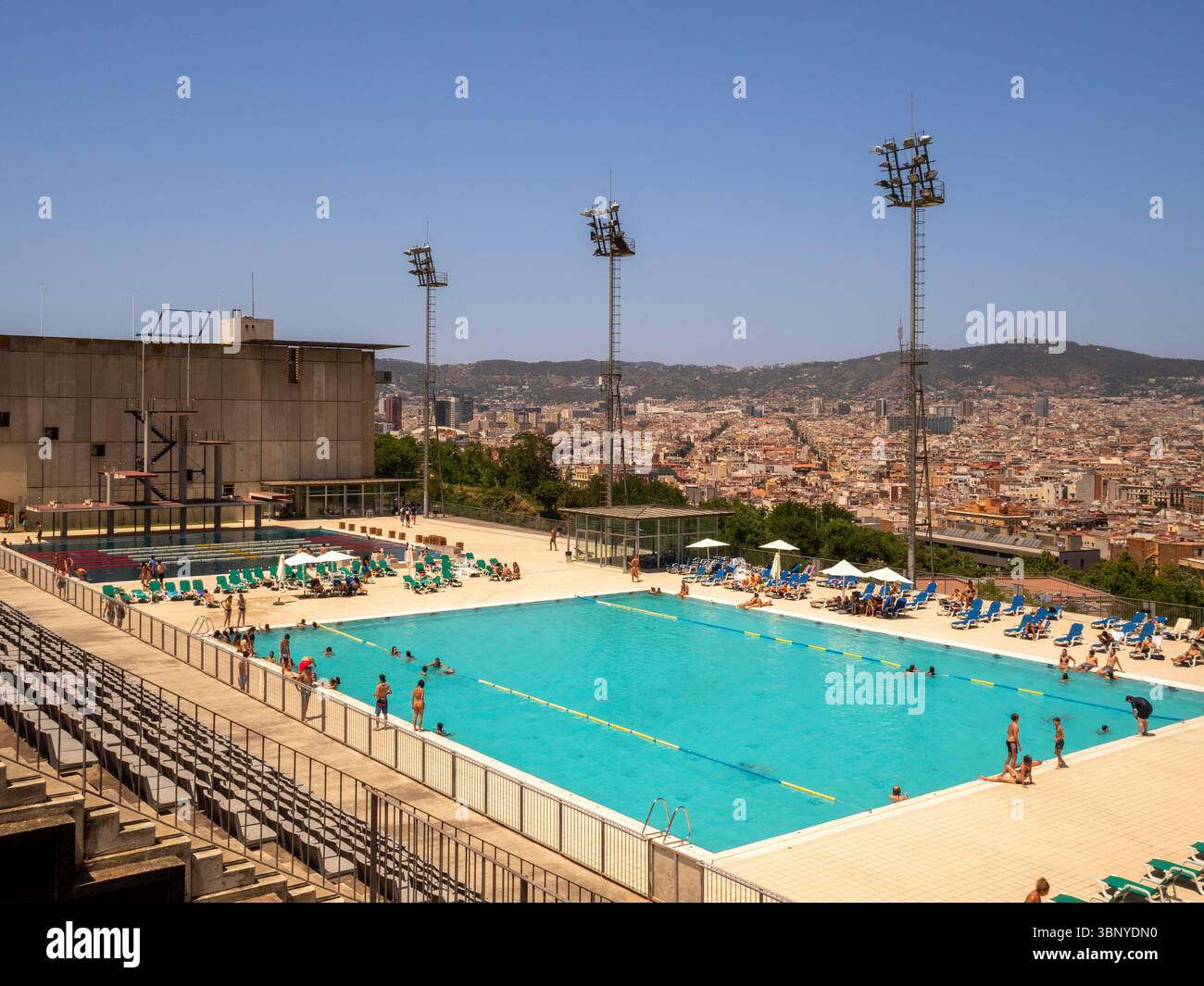Persone che apprezzano la piscina pubblica della piscina Municipal de Montjuic, una struttura olimpica del 1992 affacciata sullo skyline di Barcellona, in Spagna. Foto Stock