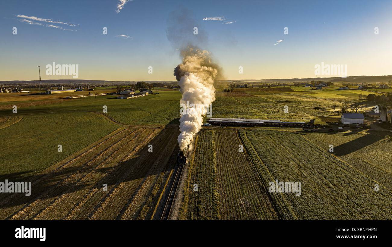 Una veduta aerea all'alba di un treno passeggeri a vapore che si avvicina soffiando molto fumo in un giorno d'autunno Foto Stock Una veduta aerea all'alba di un treno passeggeri a vapore che si avvicina soffiando molto fumo in un giorno d'autunno Foto Stock
