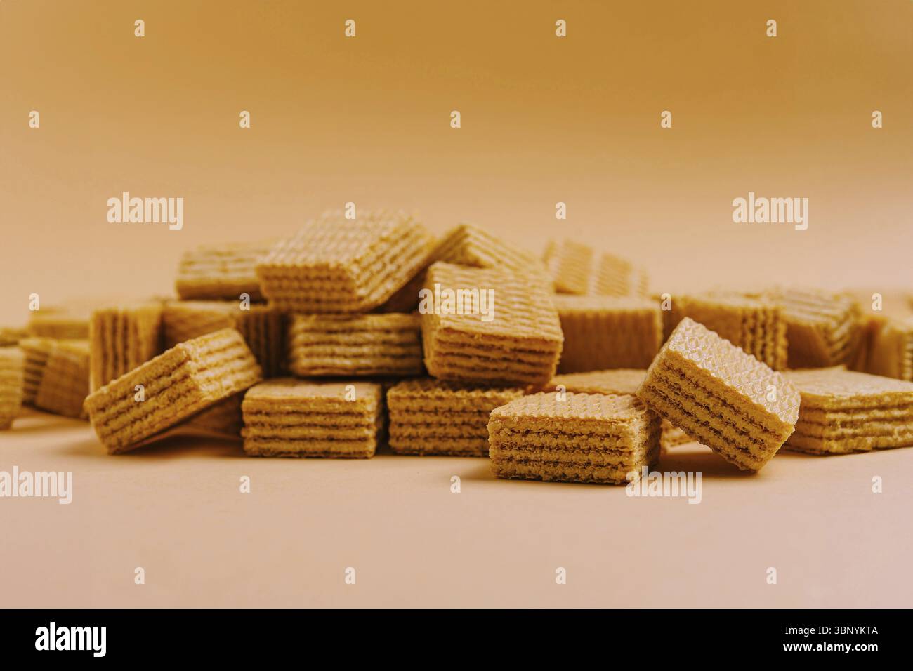 Natura morta alimentare, Un mucchio di wafer dorati con strati croccanti impilati e sparsi su una superficie beige morbida. La texture sembra invitante e perfetta per Foto Stock
