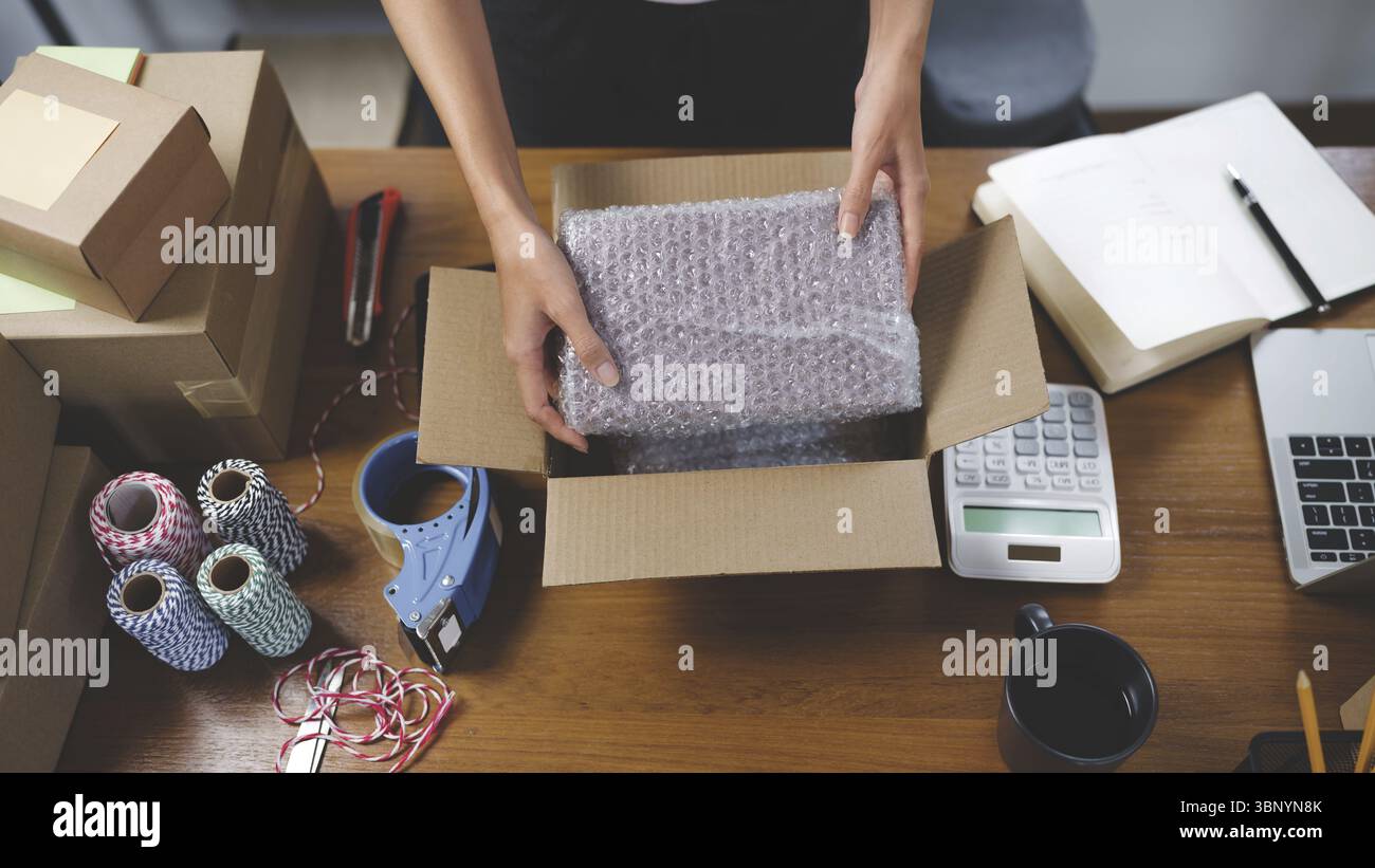 Piccolo imprenditore asiatico che imballa nella scatola di cartone preparando il pacco per la consegna online vendendo online su Internet da casa Foto Stock