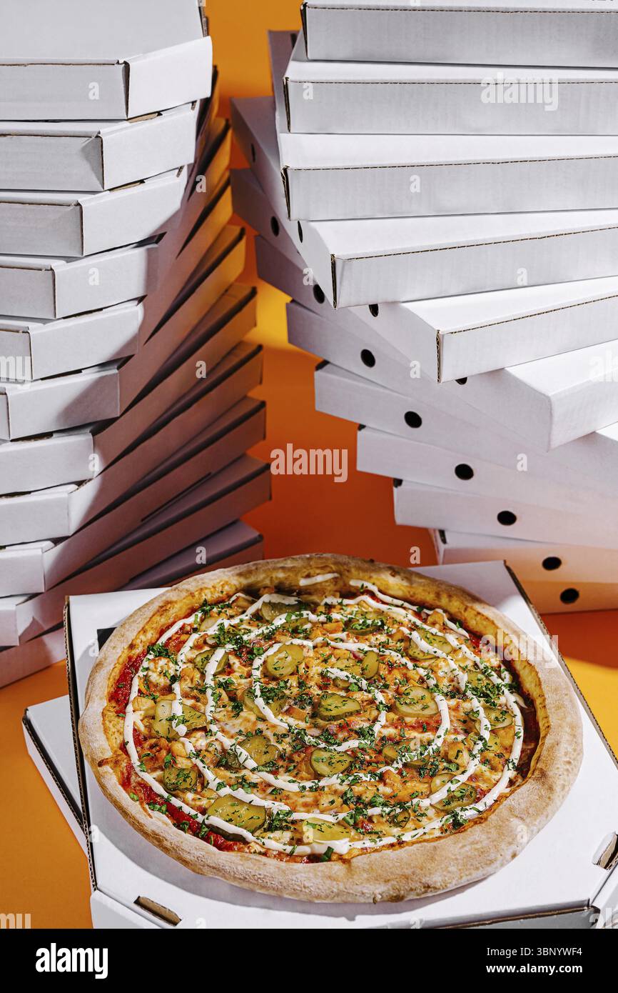 Food STILL-Life, Una pizza ben organizzata presenta una gamma di condimenti colorati, sullo sfondo di numerose scatole pizze impilate. Il bricco Foto Stock
