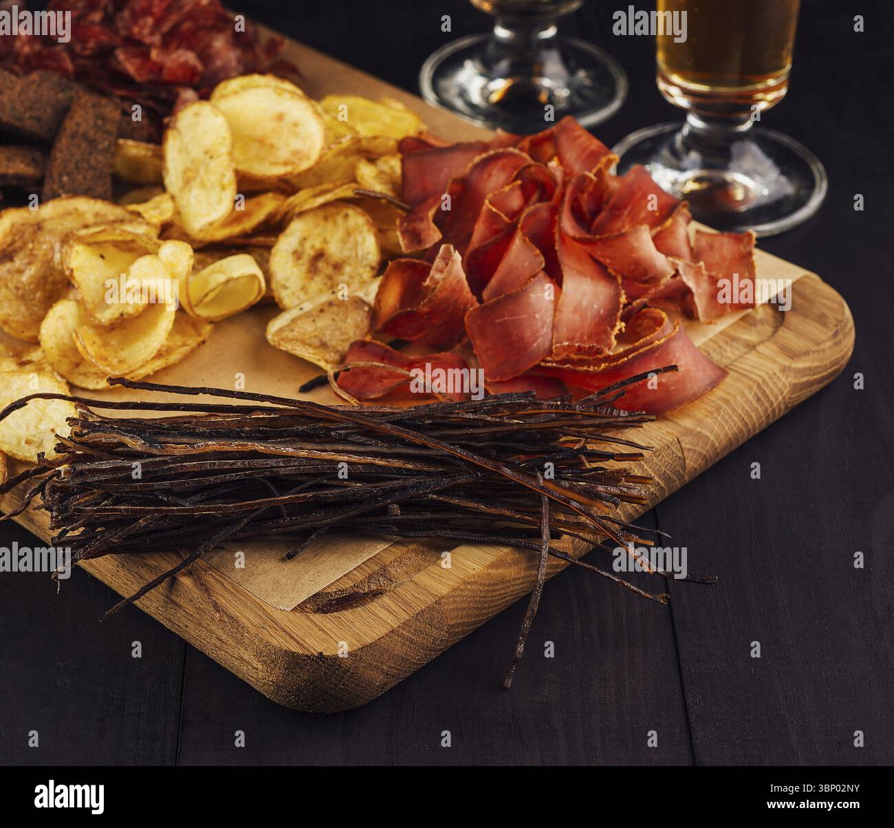 Natura morta, deliziose patatine fritte, spuntini di carne e pesce secco steso su una tavola di legno, spuntini perfetti per la birra Foto Stock