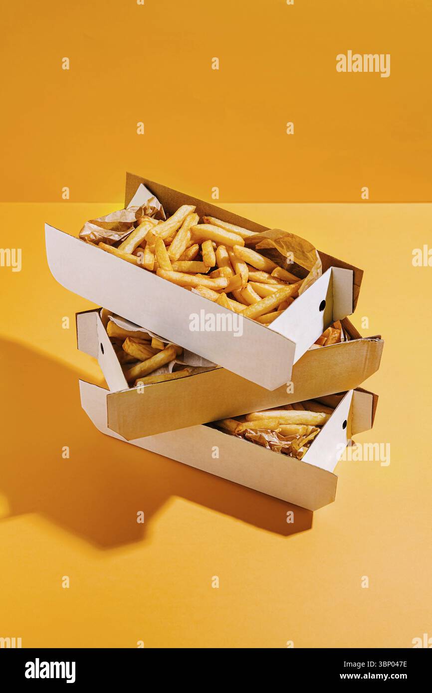 Food STILL-Life, tre scatole piene di patatine dorate e croccanti sono impilate ordinatamente con uno sfondo arancione brillante, che mette in risalto la prelibatezza del TH Foto Stock