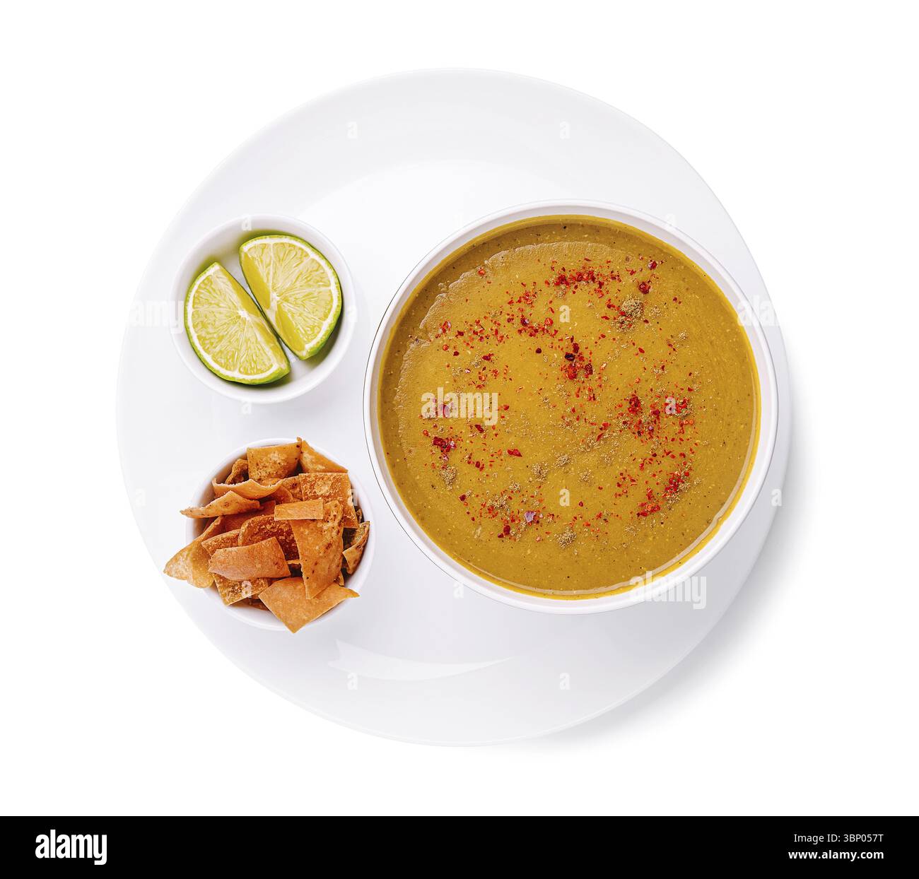 Cibo natura morta, Una ciotola calda di abbondante zuppa si trova su un piatto bianco accanto a patatine croccanti e spicchi di lime fresco. Il pasto invitante offre un delizioso e. Foto Stock