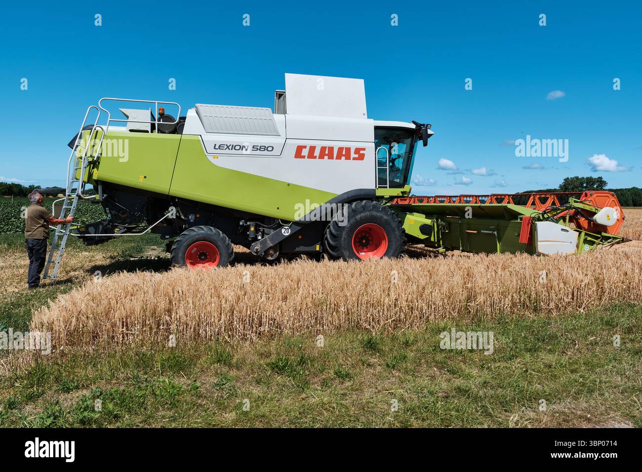 4 luglio 2025 - Patzig-Germania: Mietitrebbia Claas Lexion 580 durante la raccolta del grano, con operatore pronto a salire sulla macchina per l'ispezione sotto Foto Stock