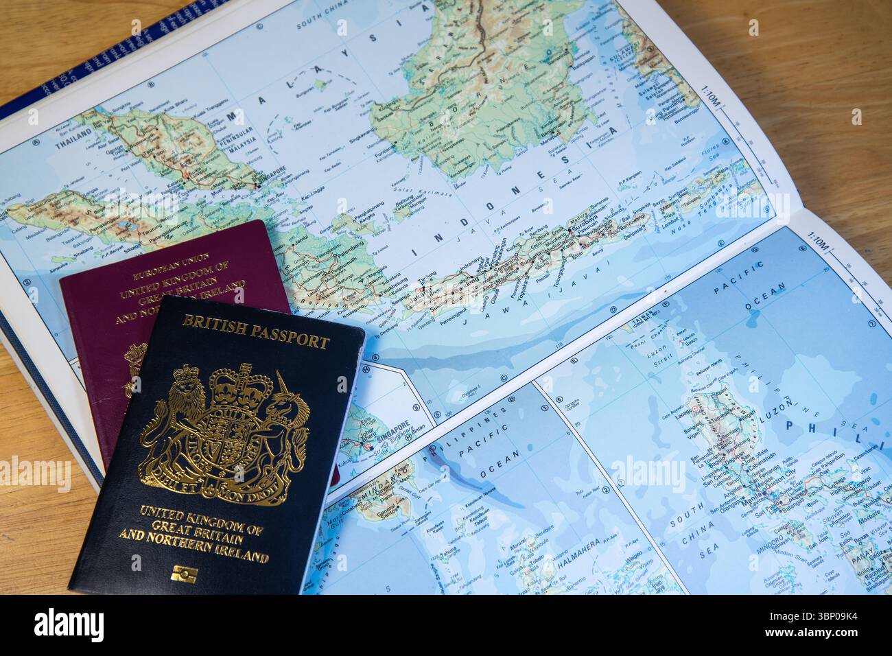 Passaporti britannici, vecchio stile UE e nuovo stile blu, collocati su un atlante a mondo aperto che mostra Malesia e Indonesia, simboleggiano i viaggi e mobili globali Foto Stock