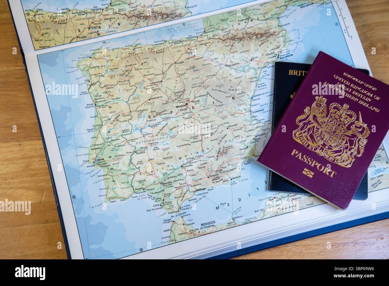 Due passaporti britannici, vecchio stile europeo e nuovo stile blu, poggiati su un atlante aperto che mostra la Spagna, che rappresenta il viaggio, l'identità e i tempi che cambiano. Foto Stock