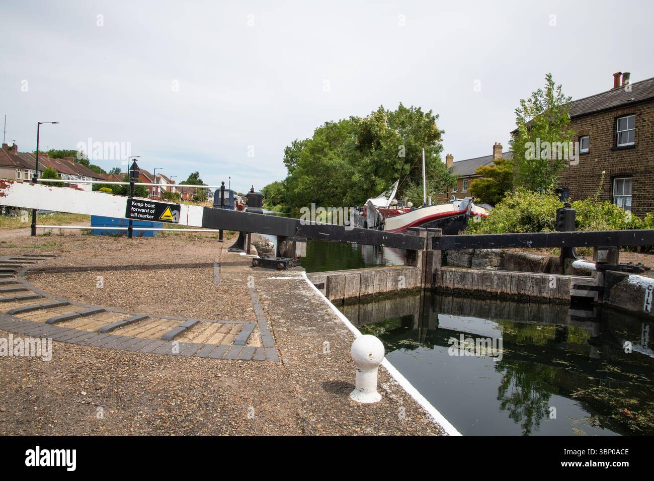 Vista di Enfield Lock sul fiume Lea Navigation, con barche sul canale, un cancello a serratura e case residenziali sullo sfondo in una tranquilla giornata estiva a Lond Foto Stock