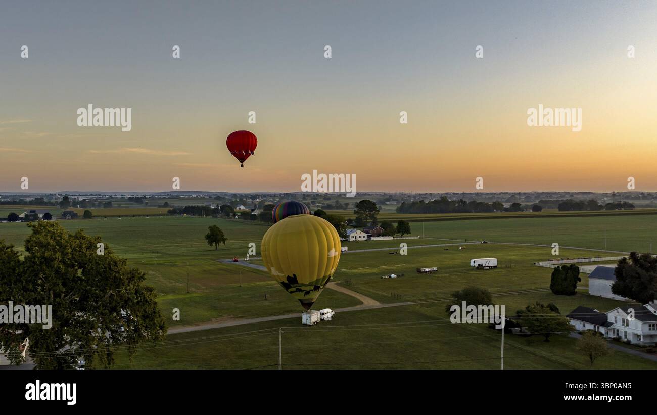 Una vista aerea di tre mongolfiere che si preparano per il lancio, con una in aria, galleggiante, in un lancio mattutino, in un giorno estivo Foto Stock