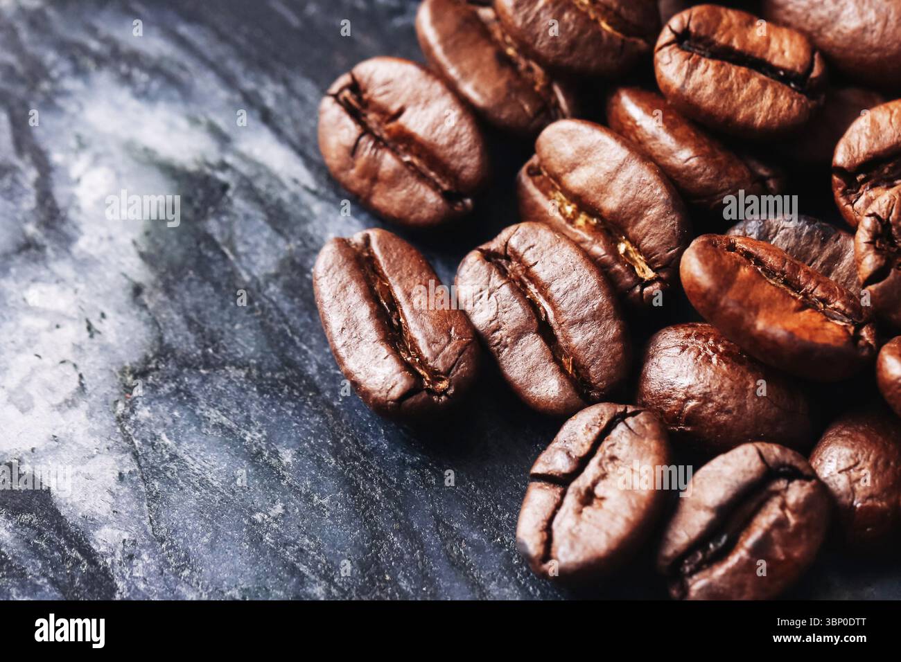 Chicchi di caffè tostati su pietra nera. Semi marroni aromatici con superficie lucida. Ingrediente naturale di caffeina per la preparazione del caffè. Consistenza macro dell'espresso. Foto Stock