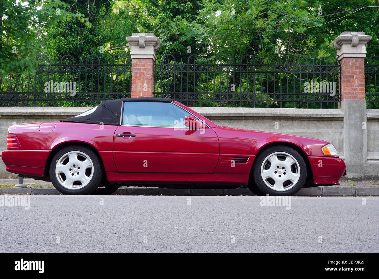 Bucarest, Romania – 11 maggio 2025: Vista laterale della Mercedes R129 SL classica cabriolet rossa Foto Stock