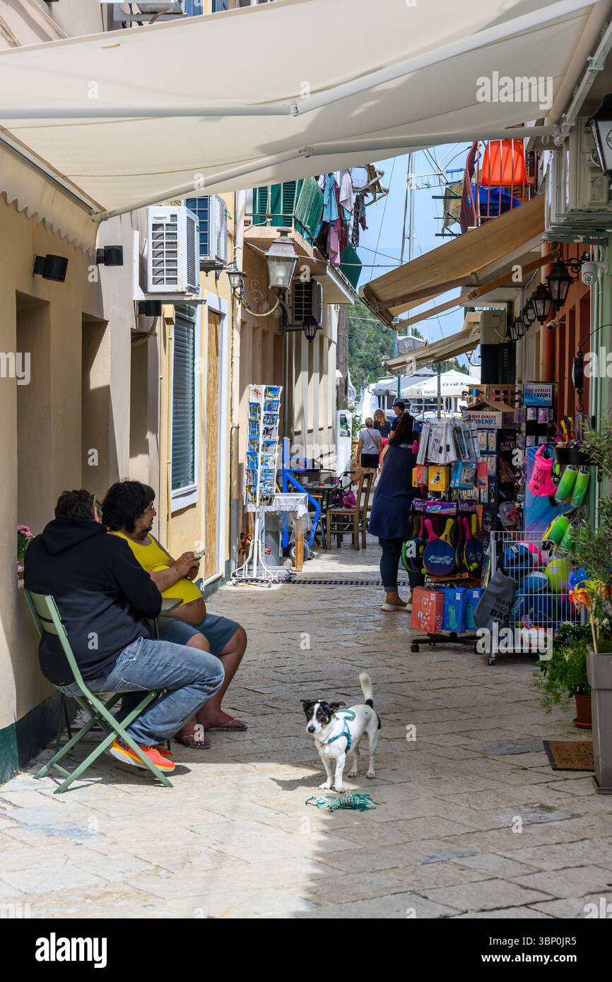 12-19/05/2025 Lakka, Paxos, Grecia. Gli abitanti del posto si godono un caffè all'ombra di una tenda, in una strada pedonale con negozi di souvenir. Foto © Simon Grosset Foto Stock