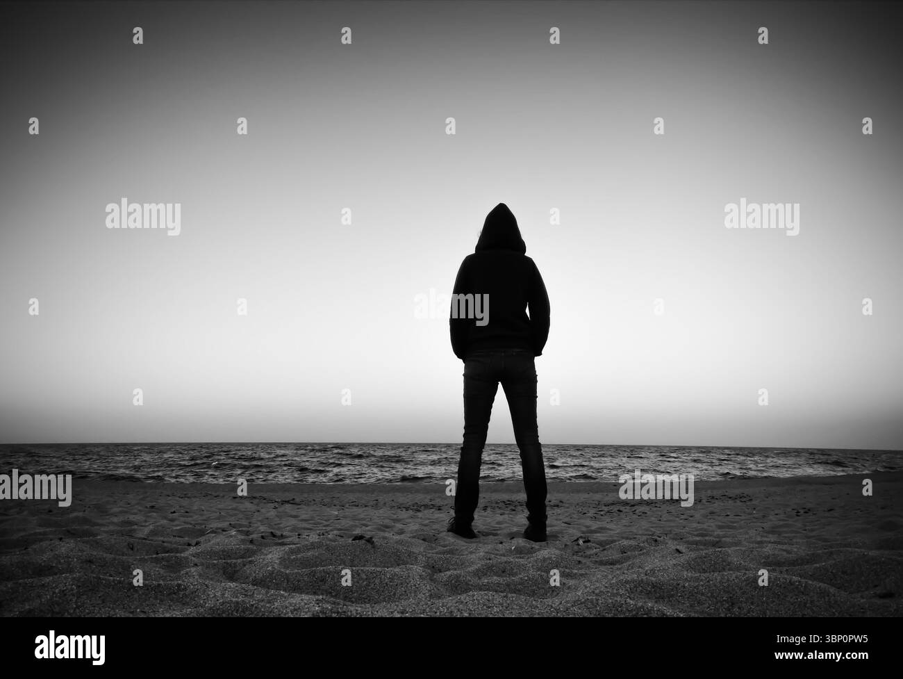 Immagine scura di una persona in piedi sulla spiaggia che guarda fuori sull'acqua. Foto Stock