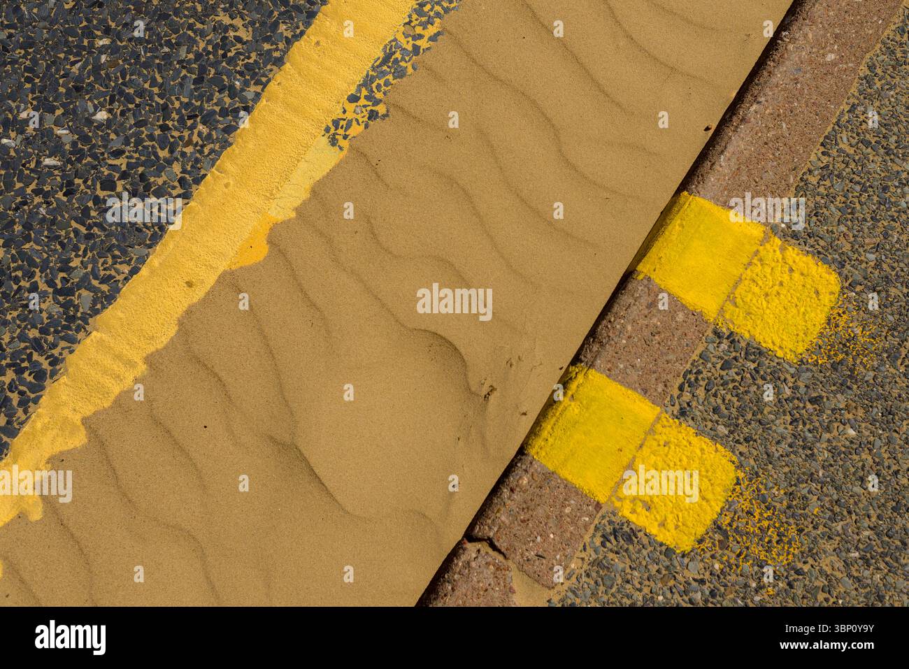 Contrassegni gialli sul marciapiede, doppie linee gialle e sabbia nel grondaiolo Foto Stock