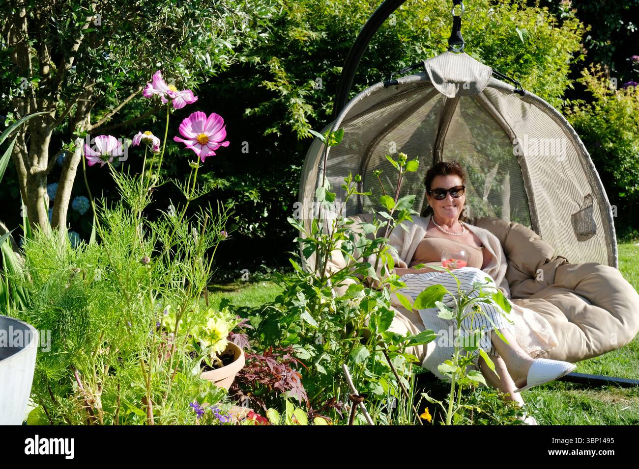 Bella donna seduta su una sedia a forma di uovo godendo della luce del sole serale - John Gollop Foto Stock