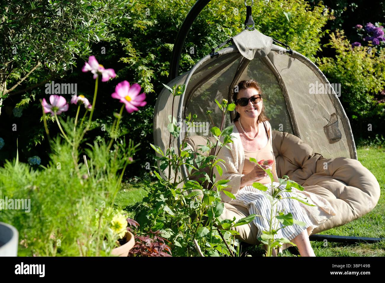 Bella donna seduta su una sedia a forma di uovo godendo della luce del sole serale - John Gollop Foto Stock