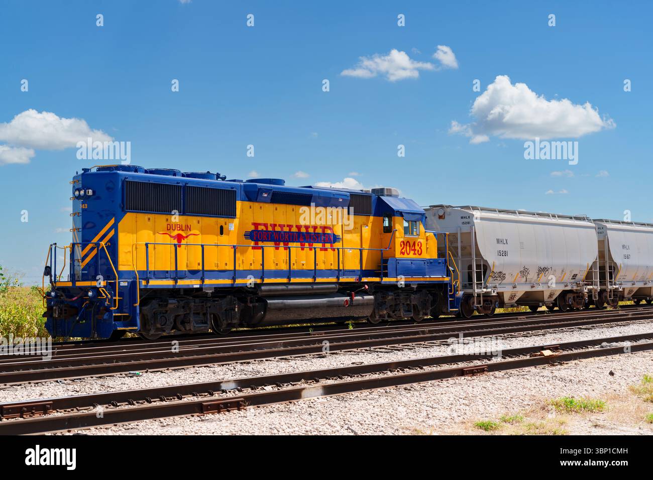 Una colorata locomotiva blu e gialla di Fort Worth e Western nel deposito ferroviario con vagoni per grano vicino a Fort Worth, Texas Foto Stock