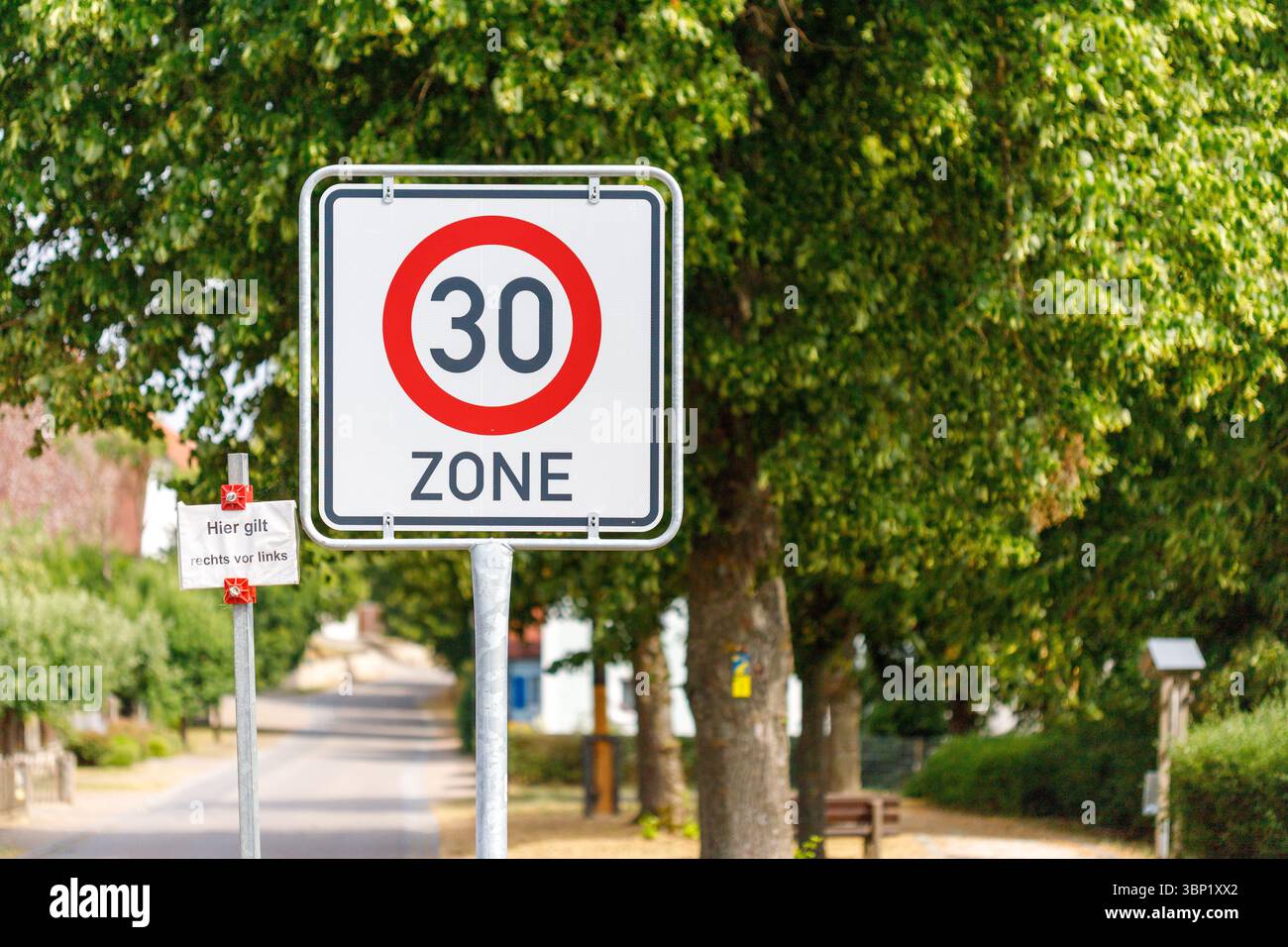 Un segnale tedesco del limite di velocità "30 zone" è ben visibile su uno sfondo di alberi verdi che costeggiano una strada in un'area residenziale.n Foto Stock