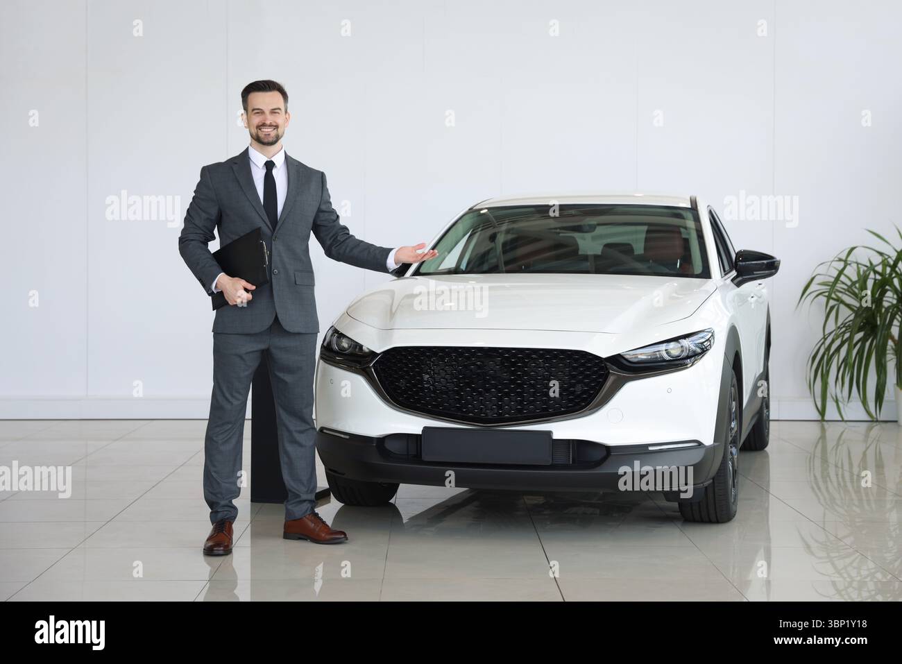Venditore sorridente con appunti che mostra la nuova auto in salone Foto Stock