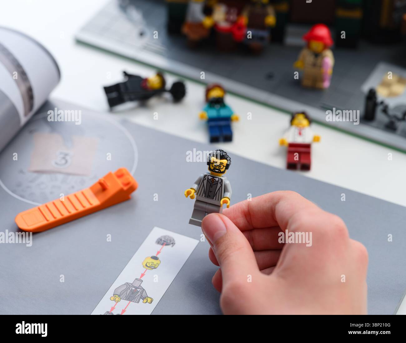 Tambov, Federazione Russa - 28 giugno 2025 Una persona con in mano una minifigura Lego costruita sopra un libretto di istruzioni. Alcune minifigure e Lego sono stati inseriti Foto Stock