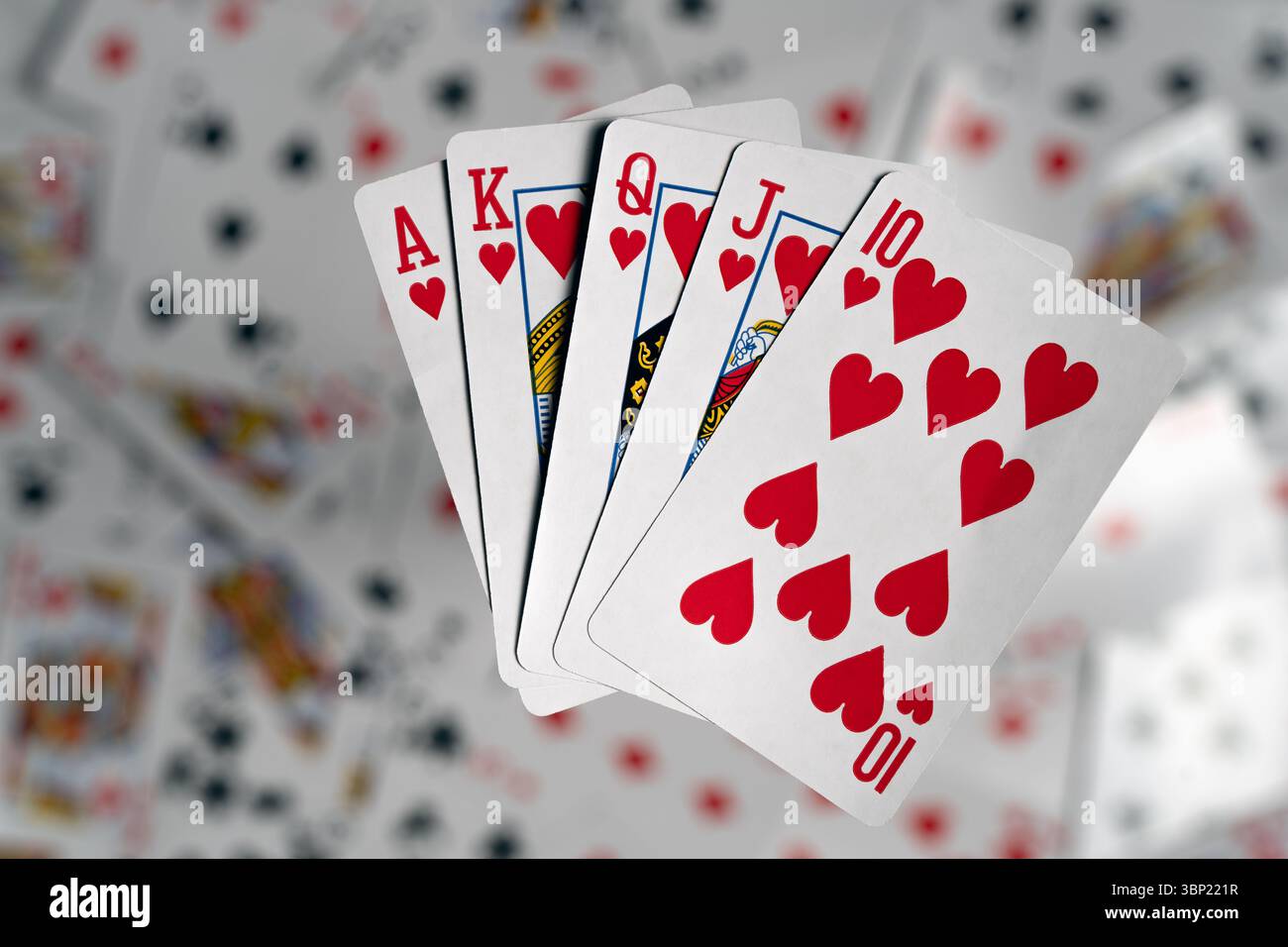 Una completa scala reale nei cuori si è sventolata e sembra fluttuare sopra uno sfondo sfocato di carte da gioco sparse Foto Stock