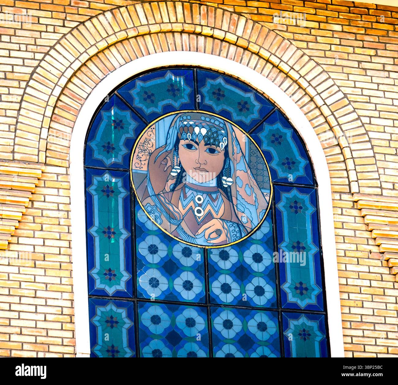 Una vetrata decorativa con un ritratto stilizzato di una donna con un abbigliamento tradizionale, circondato da motivi geometrici. I colori sono vib Foto Stock