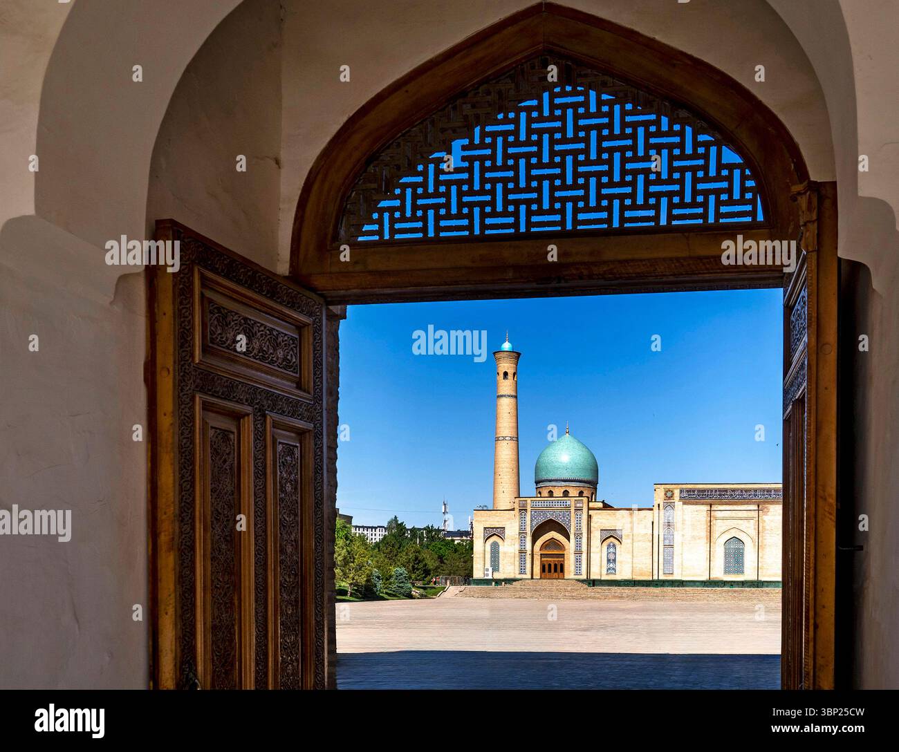 Una splendida vista di una moschea con una cupola turchese e un alto minareto, incorniciato da una porta ornata. Il cielo azzurro e limpido esalta la bellezza architettonica Foto Stock
