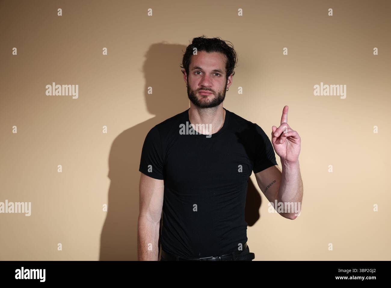 Un uomo barbuto con una t-shirt nera guarda verso la fotocamera mentre punta il dito indice verso l'alto, simboleggiando un'idea, un punto di attenzione o una mamma Foto Stock