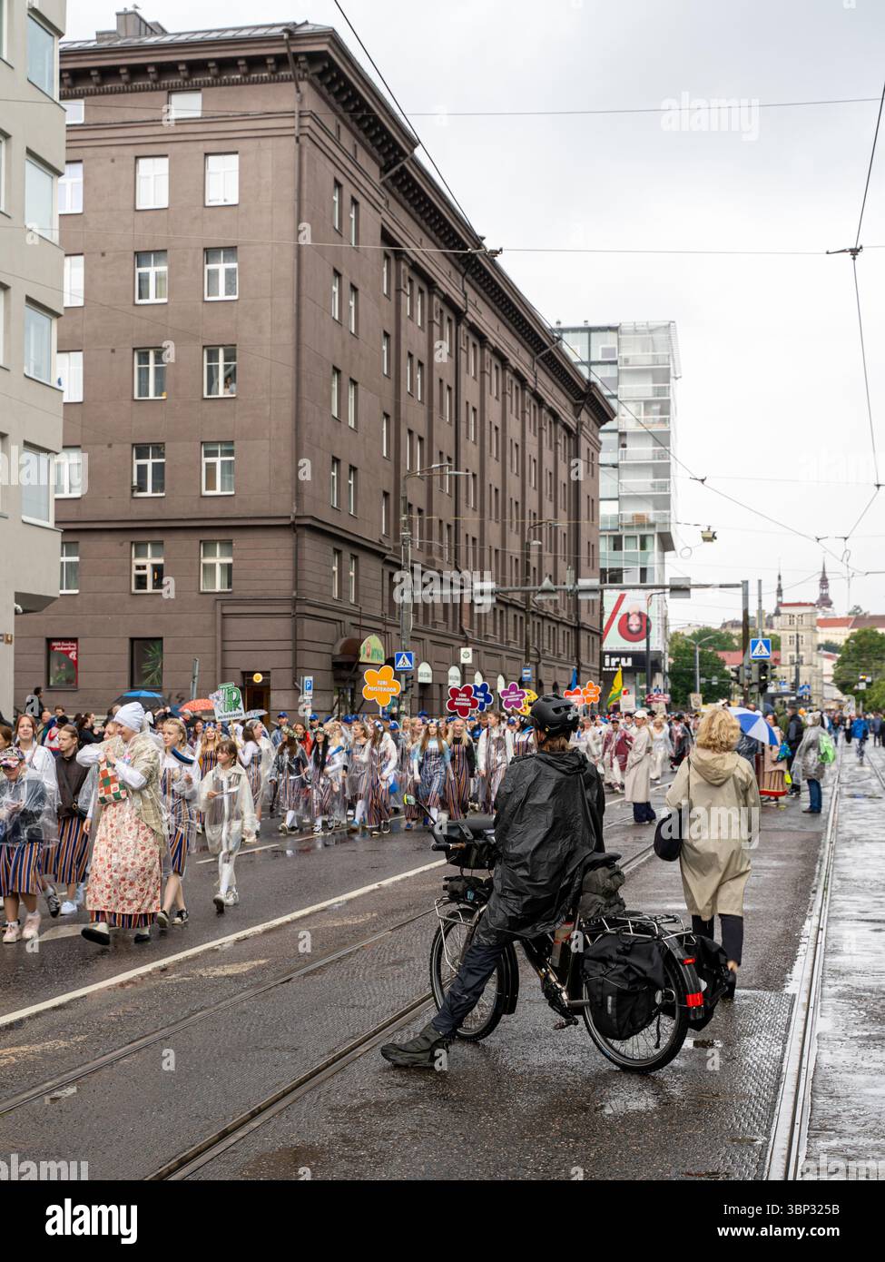 Gli spettatori e un fotografo in bicicletta osservano la processione del Festival della canzone estone nel centro di Tallinn, Estonia, luglio 2025, nonostante la pioggia Foto Stock