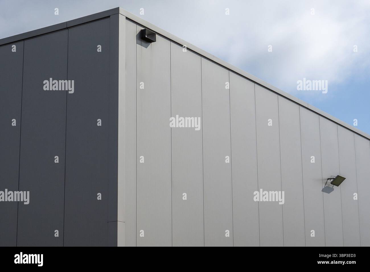 Facciata in metallo grigio di un moderno edificio industriale con luci di sicurezza sotto un cielo blu Foto Stock