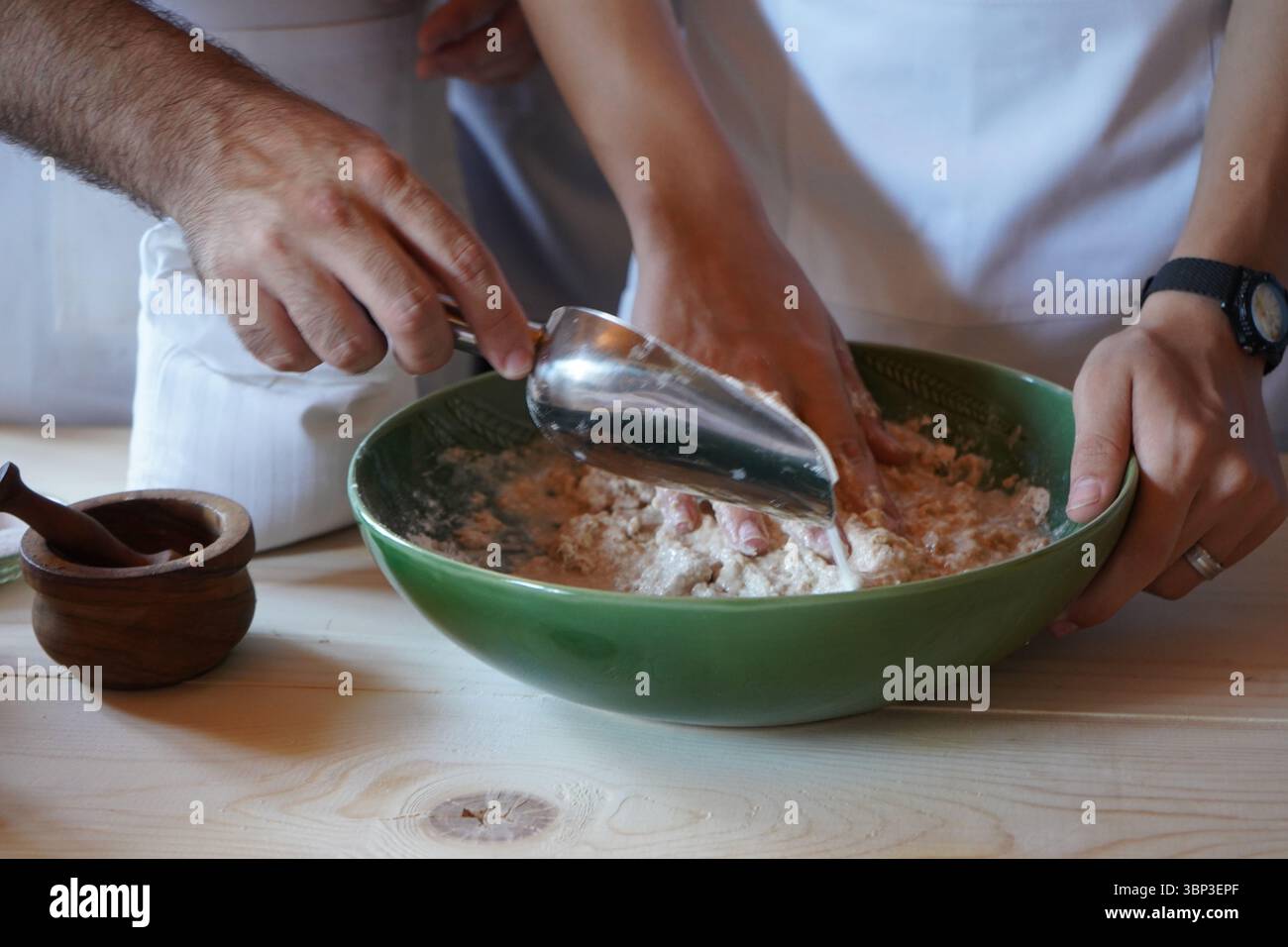 Lavorare insieme per mescolare l'impasto in una ciotola verde su un tavolo di legno: Un momento intimo e autentico di cottura e cottura da vicino. Foto Stock