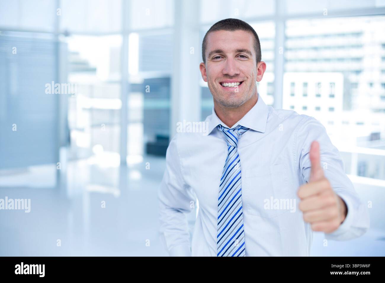 L'uomo d'affari indossa una camicia e una cravatta a righe accanto alle finestre di vetro in un ufficio luminoso Foto Stock