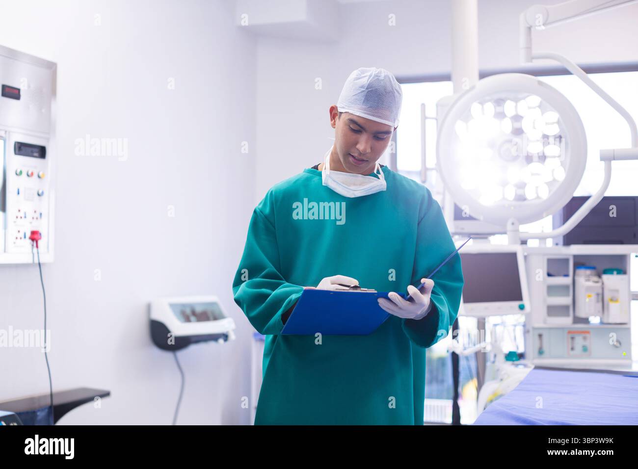 Chirurgo maschile che esamina le note sulla clipboard blu sotto la lampada chirurgica in sala operatoria Foto Stock