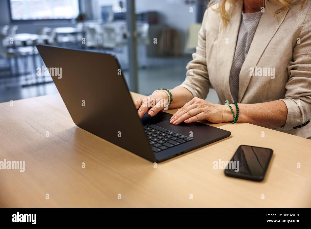 Imprenditrice donna che digita sul laptop mentre lavora alla scrivania dell'ufficio, telefono cellulare a portata di mano. Foto Stock