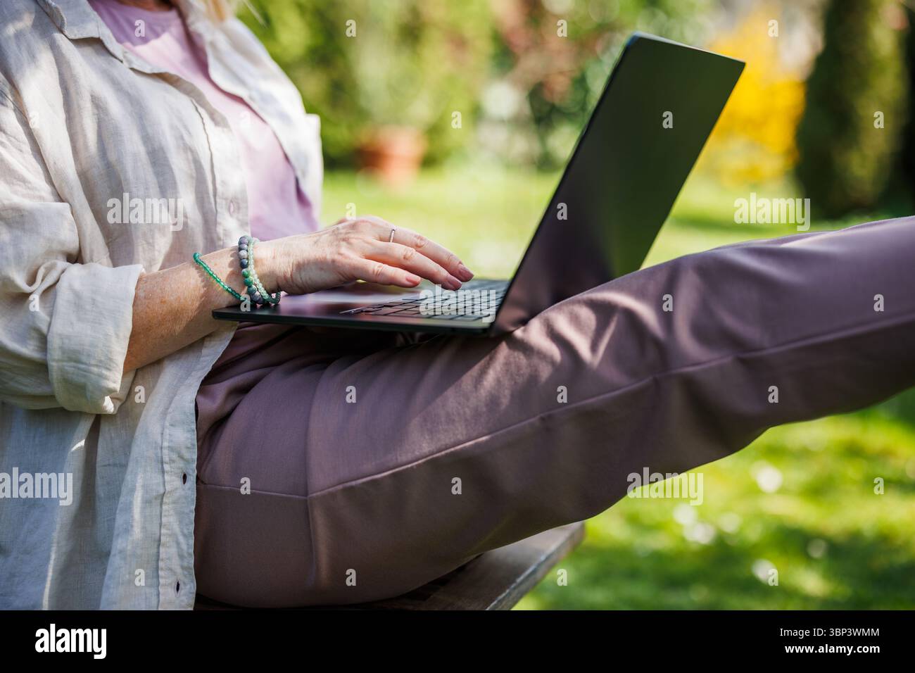 La donna sta usando un computer portatile in giardino. Le mani femminili scrivono sul notebook Foto Stock