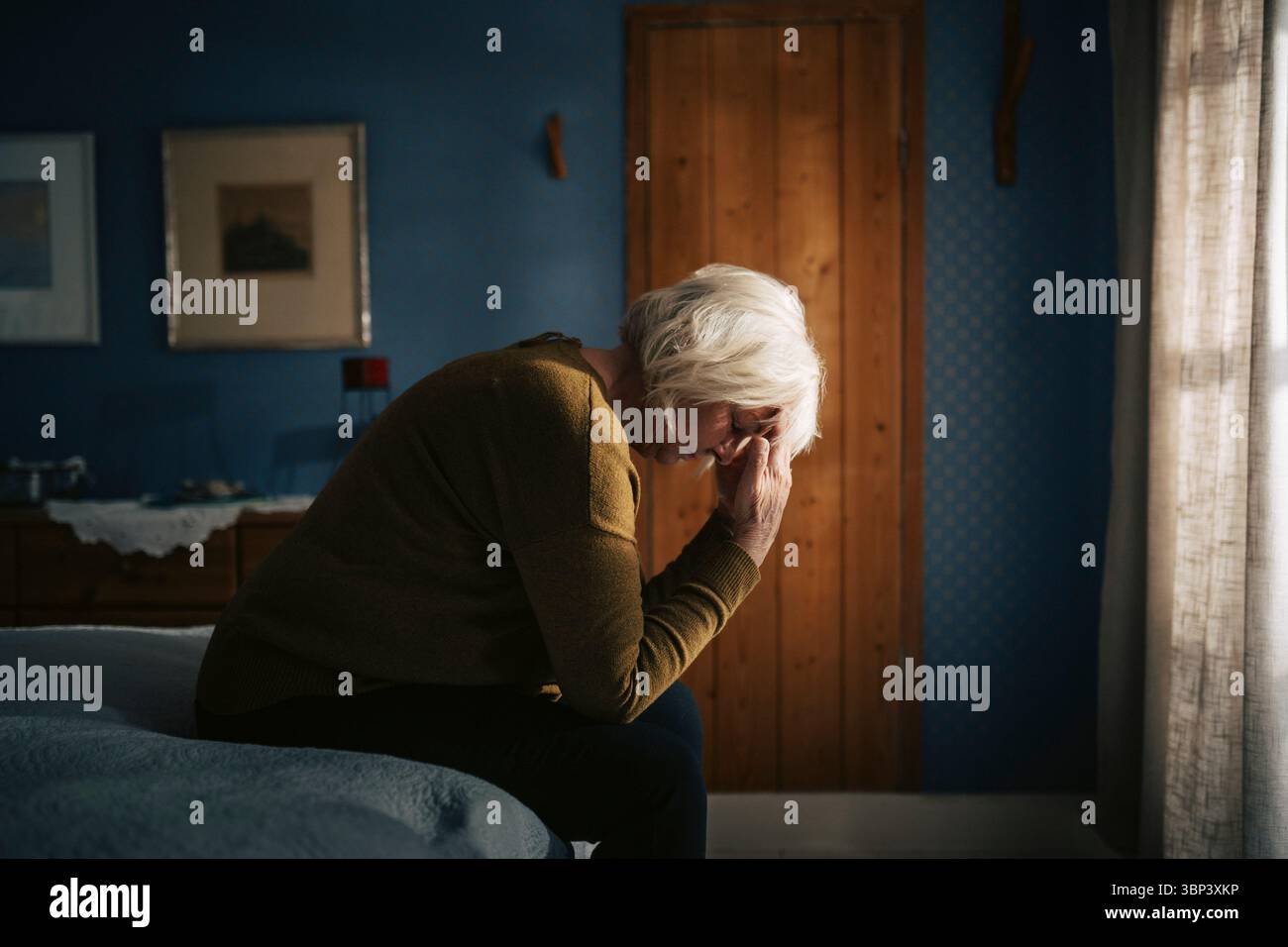Una donna anziana preoccupata seduta con la faccia in giù sul letto in camera da letto di casa Foto Stock