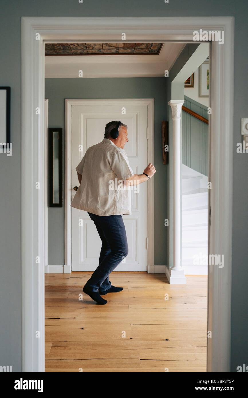 Uomo anziano spensierato che indossa cuffie wireless che balla a casa Foto Stock