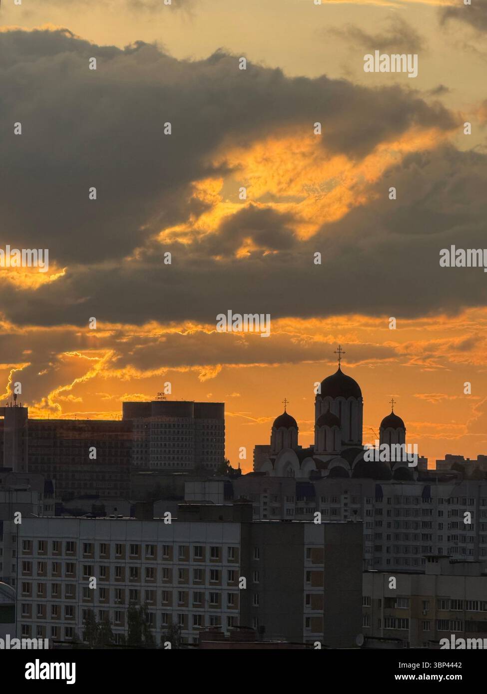 La foto cattura un paesaggio urbano durante il tramonto, con diversi edifici residenziali di media altezza e una distinta chiesa ortodossa con cupole e croci. Foto Stock