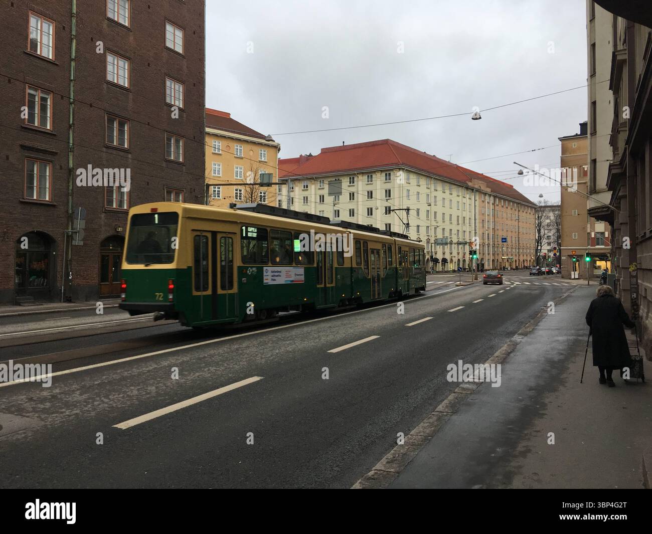 I tram si spostano attraverso le strade della città di Helsinki, mostrando le classiche carrozze verdi, le rotaie, i cavi sospesi e i dintorni urbani Foto Stock